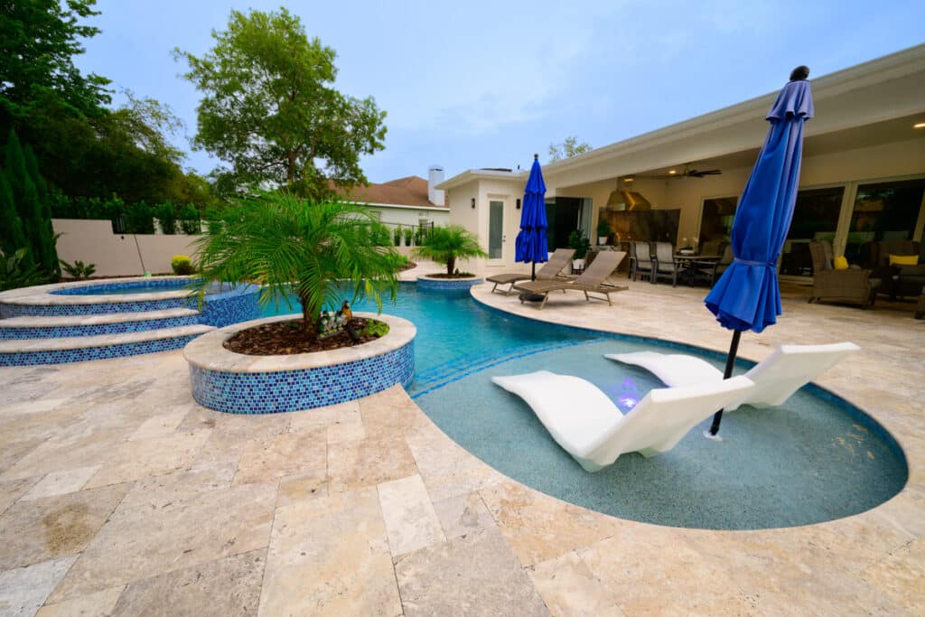 Backyard pool with blue umbrellas and lounge chairs partially submerged in the water