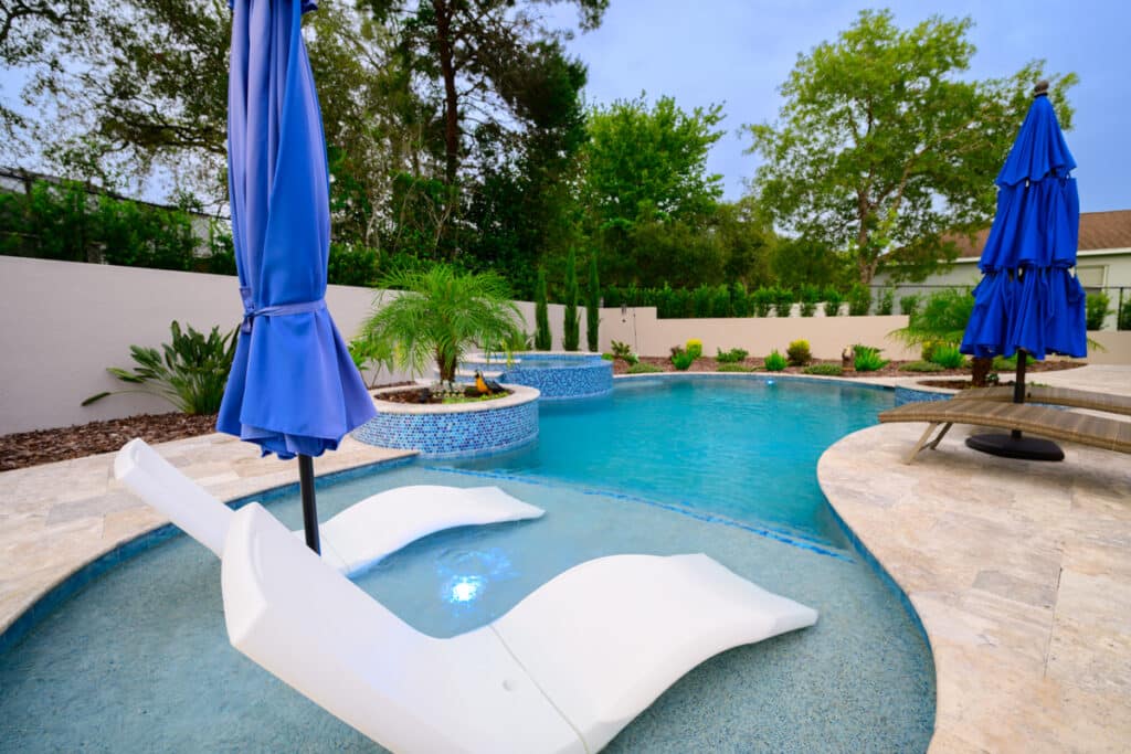 Backyard pool with submerged lounge chairs on sun shelf and blue umbrellas