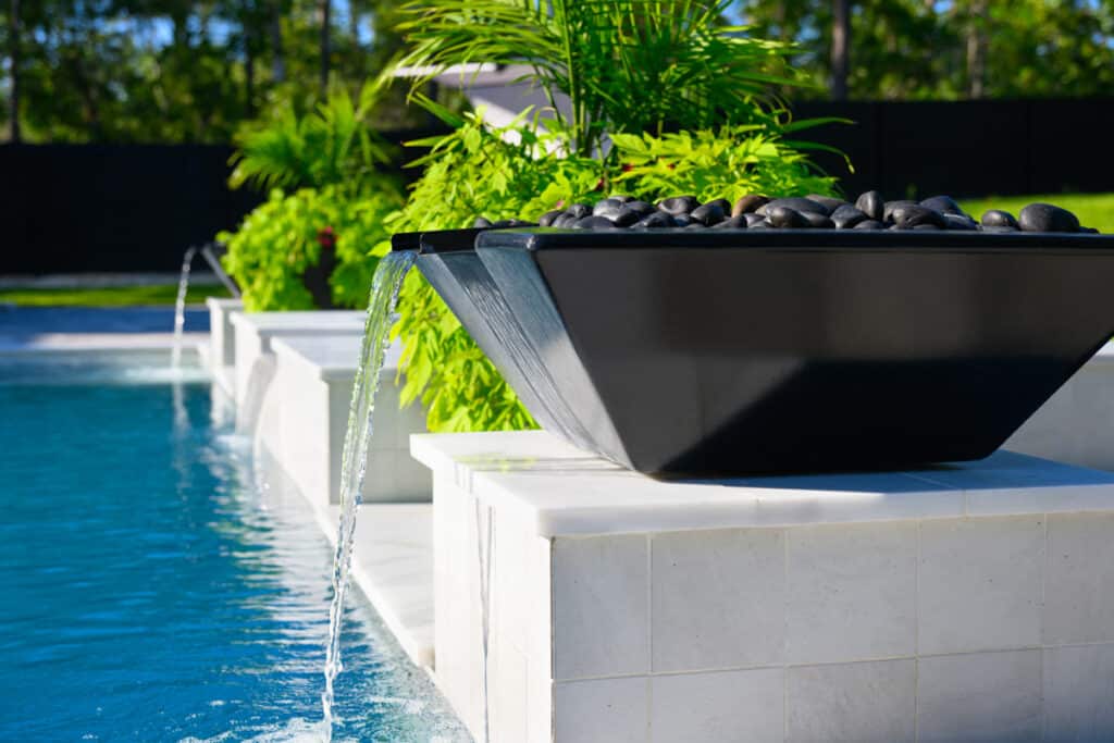 Black fire water bowl at the pool's edge, surrounded by lush greenery