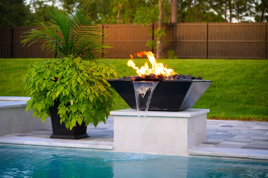 Black fire water bowl with flames, positioned next to a sleek modern pool.