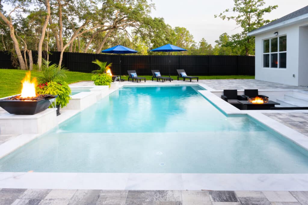 Clear blue pool with a spacious deck, surrounded by lush greenery and a serene atmosphere.