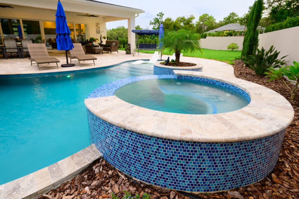 Close-up of a hot tub integrated into a backyard pool, with blue mosaic tiles and LED lighting