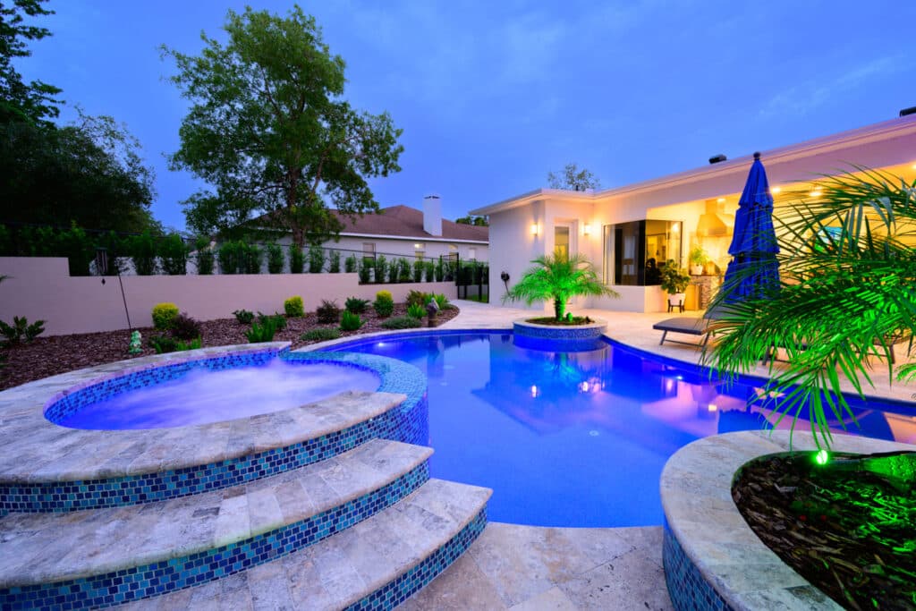 Curved backyard pool in Weeki Wachee with a hot tub, blue mosaic tiles, and integrated LED lights