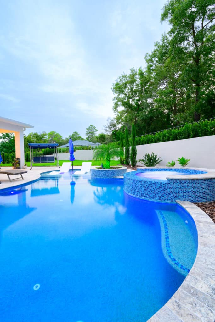 Curved backyard pool with blue mosaic tiles and lush greenery in Weeki Wachee