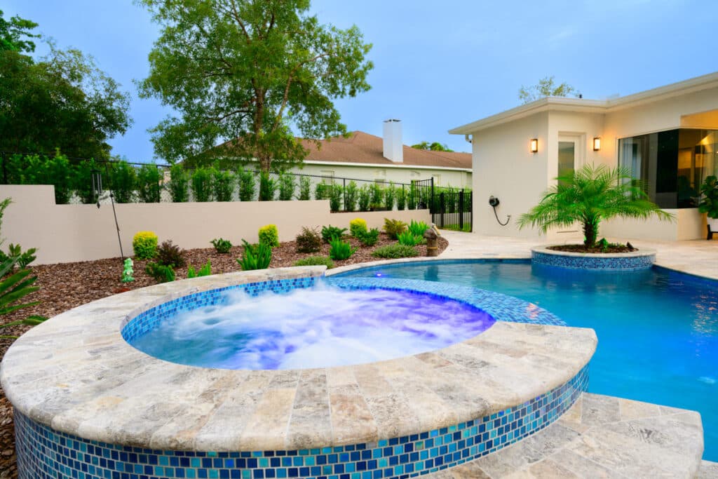 Hot tub with vibrant LED lights and blue mosaic tiles, seamlessly integrated into a Weeki Wachee backyard pool