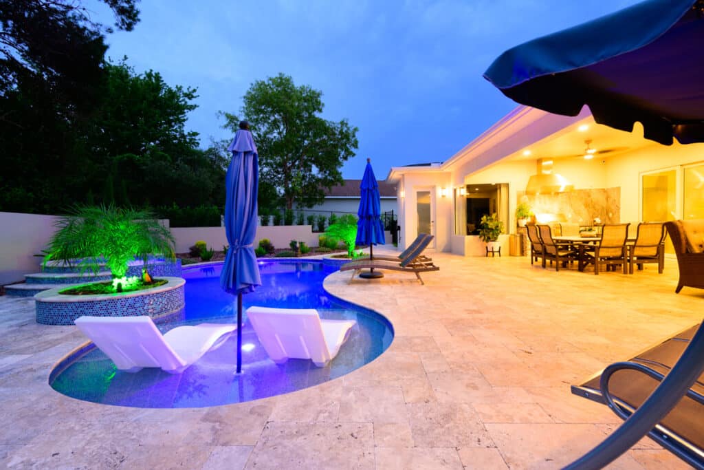 Luxurious Weeki Wachee backyard pool with integrated steps, blue mosaic tiles, and a cozy seating area illuminated by LED lights