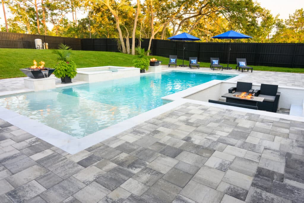 Modern pool with clean lines, surrounded by gray pavers and lush landscaping.