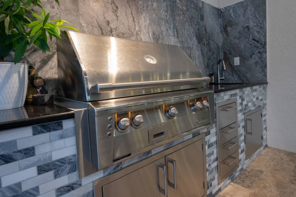 Outdoor kitchen with modern design, featuring stainless steel appliances and stone accents