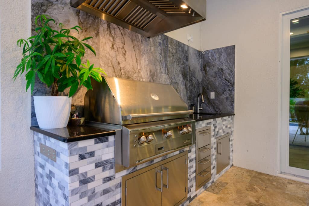 Outdoor kitchen with modern stainless steel appliances and a stylish stone backsplash