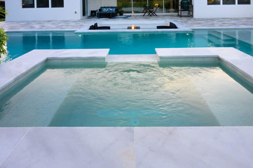 Rectangular pool with clean, clear water, featuring a sunken seating area and a black fire water bowl at one end