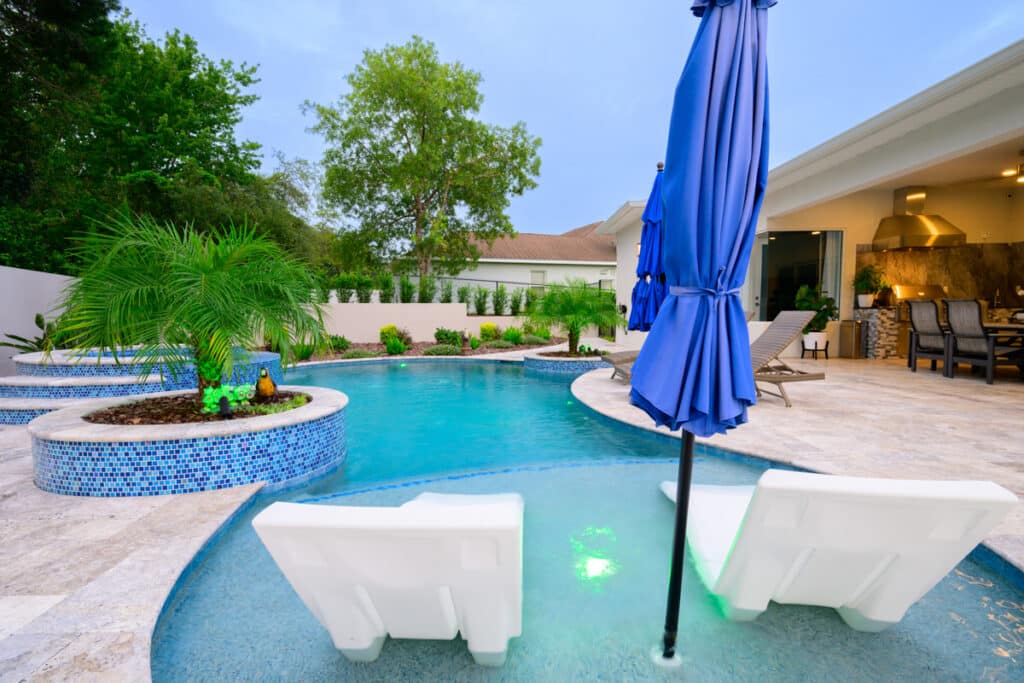 View of a backyard pool with blue umbrellas and lounge chairs