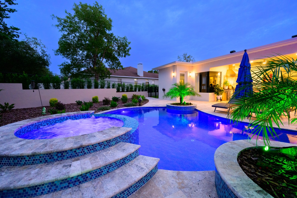 backyard pool with a circular hot tub, blue mosaic tiles, and colorful LED lights