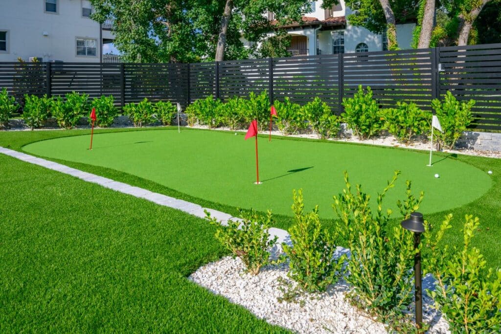 Backyard putting green with manicured grass and decorative plants.