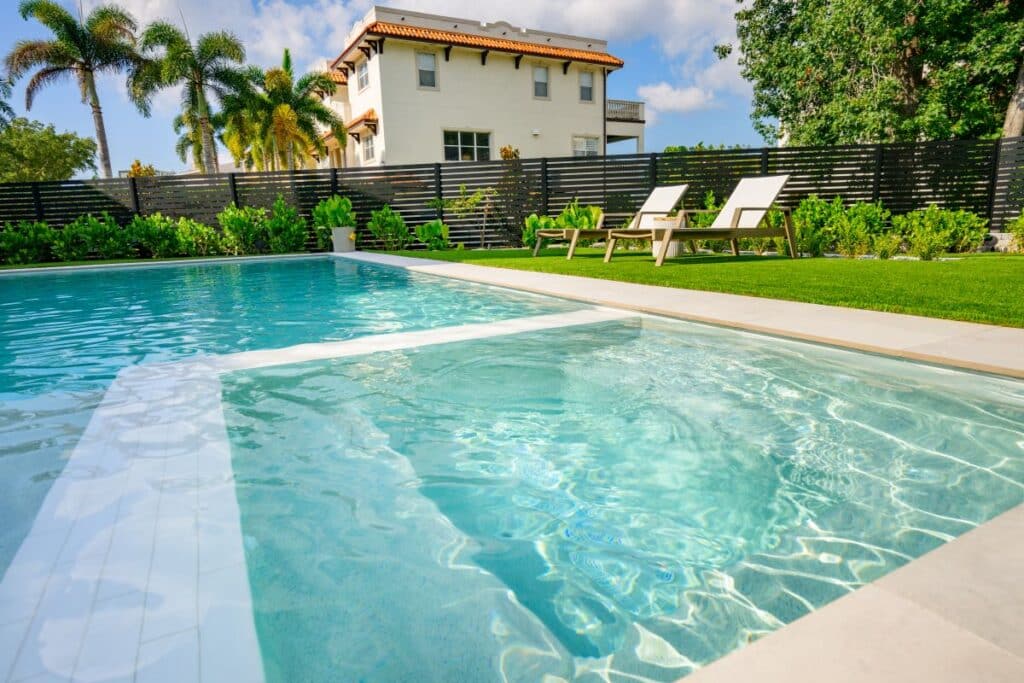 Bright backyard pool with light blue water and surrounding stone pavers.