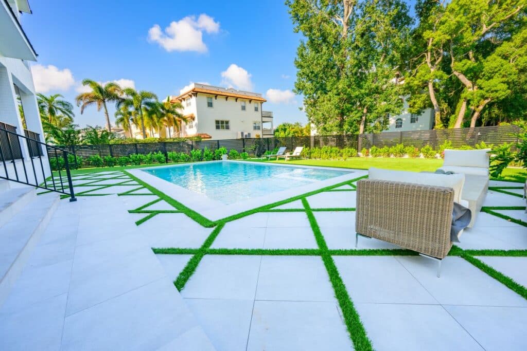 Expansive backyard with geometric paver patterns and lush landscaping around the pool.