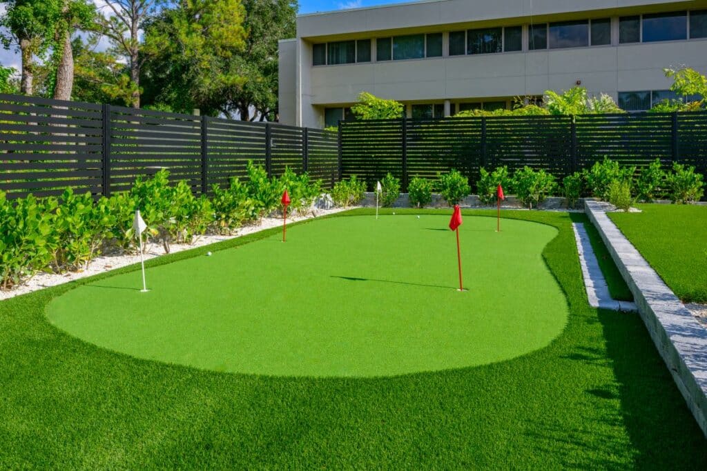 Putting green in the backyard with trimmed grass and a red flag.