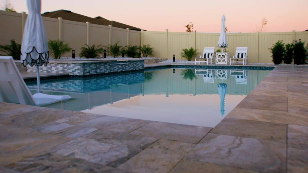 A tranquil pool area at dusk with a tiled spa and lounge chairs, surrounded by lush greenery.