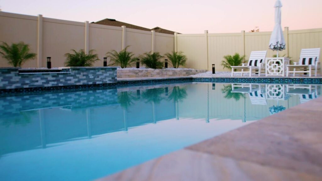 A wide-angle view of a luxurious pool with seating and dining areas, framed by travertine pavers.