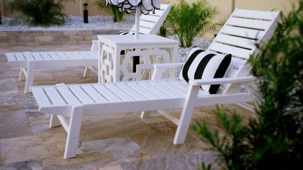 White chaise lounges with striped cushions positioned on a stone pool deck, ideal for outdoor relaxation..